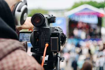 large black video camera on tripod outdoors, operator videographer shooting music festival and...