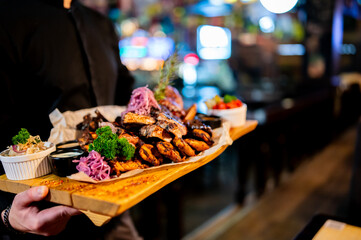 A hearty, assorted grilled meat platter with ribs, potatoes, and salad is held by a server in a dimly lit restaurant.