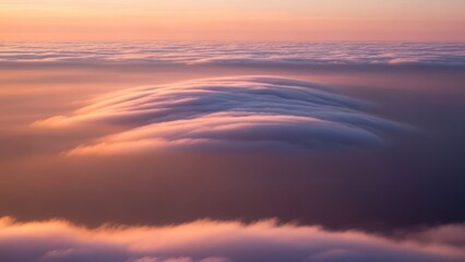 Fototapeta premium Wispy clouds glow in soft pastel sunset light above a sea of fog