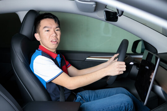 An Asian teenager sits in the driver's seat looking back while reversing, ideal for teen driving safety, parking practice, or driver education concepts.