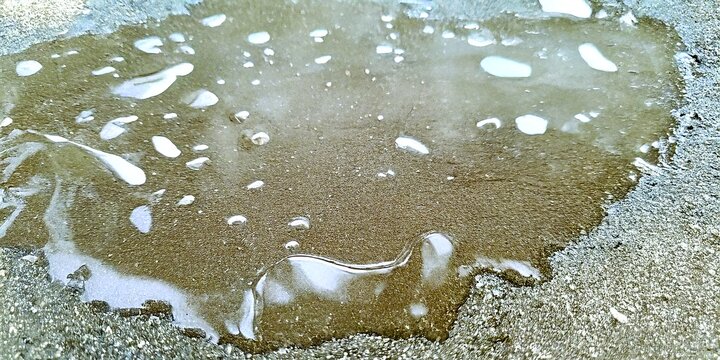 Puddle of dirty water on a concrete surface with bubbles.