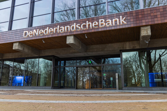 Exterior entrance of the De Nederlandsche Bank headquarters, featuring the bank's logo text above glass sliding doors and brown brick facade. Amsterdam Netherlands, 28 december 2025