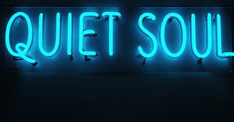 Bright blue neon sign displays words quiet soul against dark background. Simple typography creates calming visual impact.