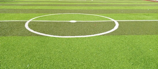 Obraz premium High-resolution image of the white center circle marking on a synthetic football turf field with alternating green stripes, ideal for sports visuals, backgrounds, and marketing use