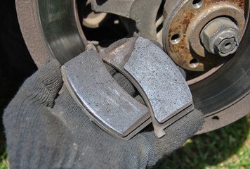 Close-up of a mechanic's gloved hand holding worn-out brake pads against a car brake disc background. mechanic showing old damaged brake pads before replacement.  © Dmytro