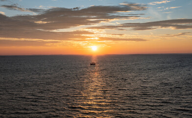 A fishing boat sails in the warm morning sunbeam through the Norwegian Sea at sunrise. Warm morning light shines over the water, creating a bright scene for shrimp fishing.
