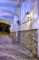 Charming stone wall with warm lantern lighting under an arched entryway at night. Elegant architectural details and cozy ambiance in this inviting, cobblestone-lined outdoor scene.