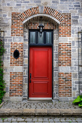 Front view of a vibrant red door set in a rustic brick and stone facade with arched frame and black lantern, showcasing traditional architecture in Old Quebec.