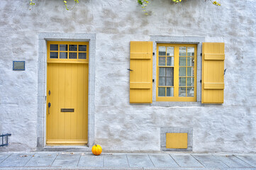Charming old stone building with a vibrant yellow door and shutters, a small pumpkin at the entrance, evoking a cozy autumn feel. Perfect for themes like architecture, heritage, or seasonal design.