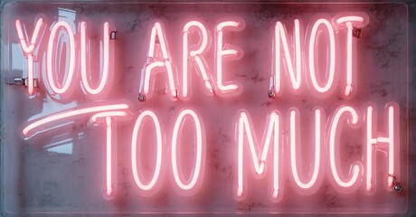 Fototapeta premium Pink neon sign displays positive message. Text reads You are not too much on textured surface, dark background.