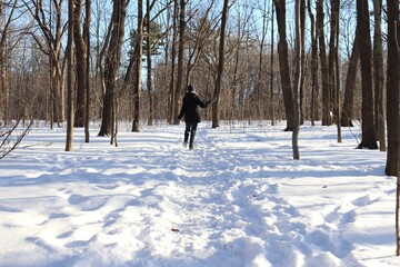 A woman in a path in winter. Forest with snow and someone walking. Hiking and trail in winter and outdoor activities. Relaxing in the forest in winter.