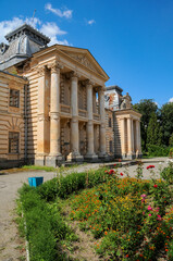 Obraz premium Koropets Palace in Ternopil region, Ukraine, ornate neoclassical facade and columns slowly crumbling amid overgrown gardens under a bright summer blue sky, forgotten estate memory