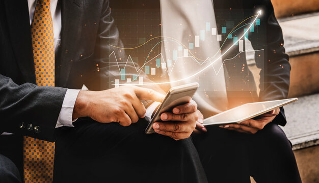 Business professionals engage in financial analysis using a smartphone and tablet, showcasing digital graphs and data trends in a modern workspace. Impute - Powered by Adobe