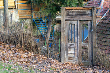 Old wooden door near a rustic building surrounded by fallen leaves and dry grass in a quiet rural area