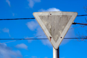 Traffic sign indicating yield posted on a street under a blue sky with some clouds in the background