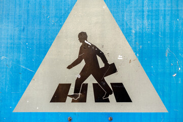 Warning sign showing pedestrian crossing with person carrying a briefcase in a city environment near road