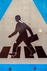 Sign shows a person walking with a briefcase across a pedestrian crossing in an urban area
