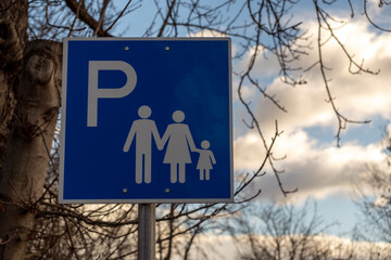 Sign for family parking spot located in a public area with trees and clouds in the background