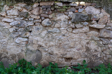 Weathered stone wall shows layers of texture and color with greenery at the base in a historical location