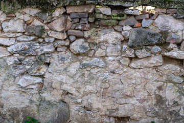 Old stone wall with uneven texture and moss growing in some parts during daylight hours in a rural setting