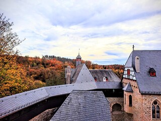 Autumn period. View of the roof of the medieval Burg castle in the old town of Solingen Germany. In the background are hills with trees in autumn bright foliage and blue cloudy sky. Natural European .