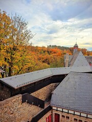  View of the roof of the medieval Burg castle in the old town of Solingen Germany. In the background are hills with trees in autumn bright foliage and blue cloudy sky. 