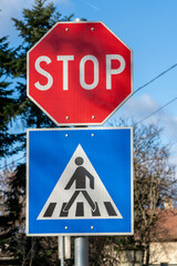 Stop sign and pedestrian crossing sign placed on the street in a residential area during daytime with blue sky