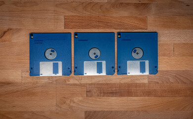 Three blue floppy disks on wooden desk surface.