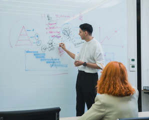 team meeting in modern office where male present stand clap while team member seat around table join. whiteboard background display triangle diagram bar chart emphasizing collaboration professional
