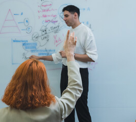 team meeting in modern office where male present stand clap while team member seat around table join. whiteboard background display triangle diagram bar chart emphasizing collaboration professional