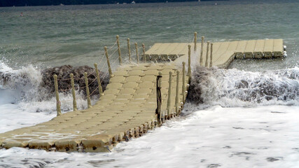 Floating plastic dock on a wavy sea with crashing waves, capturing the raw power of nature and turbulent sea conditions. © CanYalicn