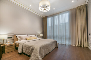 This space features a bed with light bedding and pillows, wooden furniture, and a large window...