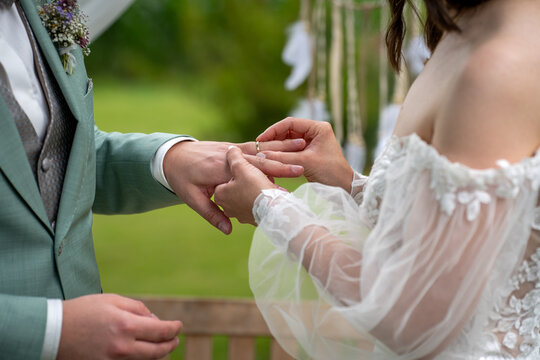 Ringtausch mit dem Anstecken des Ehering durch die Braut beim Br&auml;utigam w&auml;hrend der Trauung im Rahmen einer Hochzeit, freie Trauung drau&szlig;en 