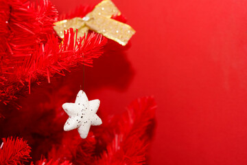 Decorative white star ornament hanging from red Christmas tree on bright background