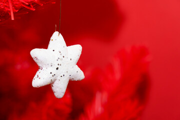 White star ornament hangs on red Christmas tree branch during holiday season