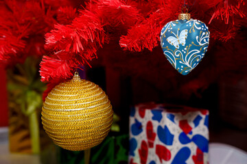 Bright ornaments hang on a red Christmas tree beside colorful wrapped gifts
