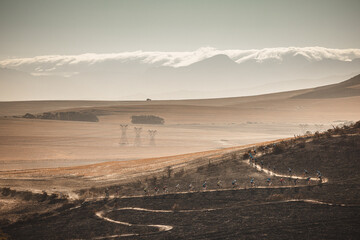 A long line of mountain bikers snakes up a dusty, winding trail during the race. Set against a hazy backdrop of layered mountain ridges and rolling hills, the scene highlights the grueling endurance