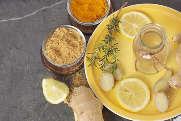 Still life scene with two small dishes containing turmeric and ginger, pieces of ginger, lemon...