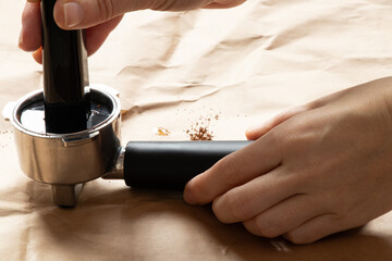 A woman's hand tamps coffee into a coffee horn with a measuring spoon on brown paper, making coffee