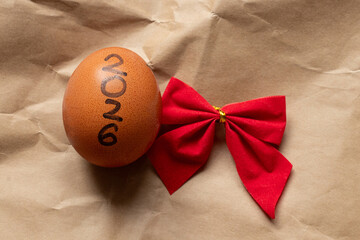A brown chicken egg with the inscription 2026 and a red bow lies on crumpled craft paper as a symbol of the New Year, time
