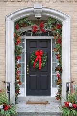 Front door decorated with holly berry and Christmas wreath with red bow