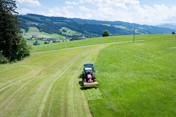 Landwirt in Bayern m&auml;ht Gras und erntet es in einem Arbeitsgang mit einem Ladewagen, Luftbild.