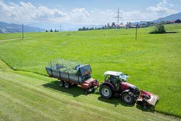 Landwirt in Bayern m&auml;ht Gras und erntet es in einem Arbeitsgang mit einem Ladewagen, Luftbild.
