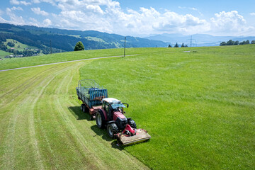 Landwirt in Bayern m&auml;ht Gras und erntet es in einem Arbeitsgang mit einem Ladewagen, Luftbild.