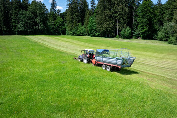 Landwirt in Bayern m&auml;ht Gras und erntet es in einem Arbeitsgang mit einem Ladewagen, Luftbild.