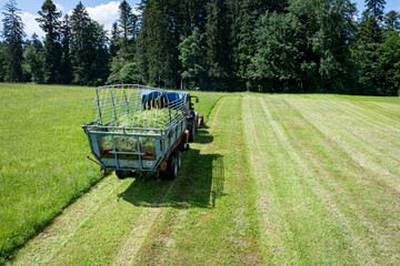 Landwirt in Bayern m&auml;ht Gras und erntet es in einem Arbeitsgang mit einem Ladewagen, Luftbild.