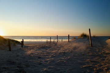 Sunset over sandy dunes leading to the calm ocean &ndash; tranquil beach landscape