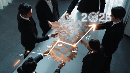 A team of professionals collaborates around a table with wooden gears and digital graphs, symbolizing innovative strategy development for future business success in 2026. Raster