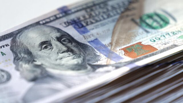 Close-up of stacked hundred-dollar bills showcasing intricate details of currency design, highlighting textures, colors, and patterns in a visually engaging manner with copy space