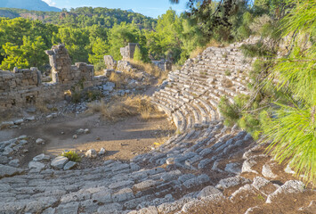 Ancient amphitheater ruins at the Ancient City of Phaselis in Tirki, surrounded by trees and rocky terrain, showcasing historical architecture and natural beauty